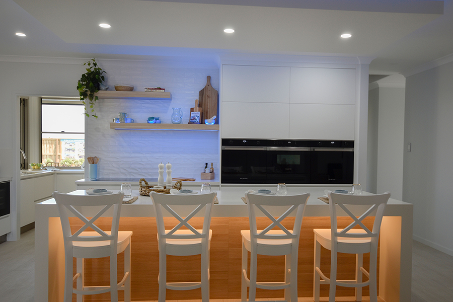 Modern white kitchen and dining area with orange-lit island, bar stools, and built-in appliances