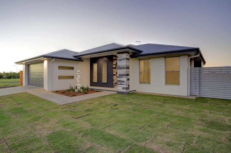 Modern single-story house with a dark roof, beige exterior, and front lawn at dusk