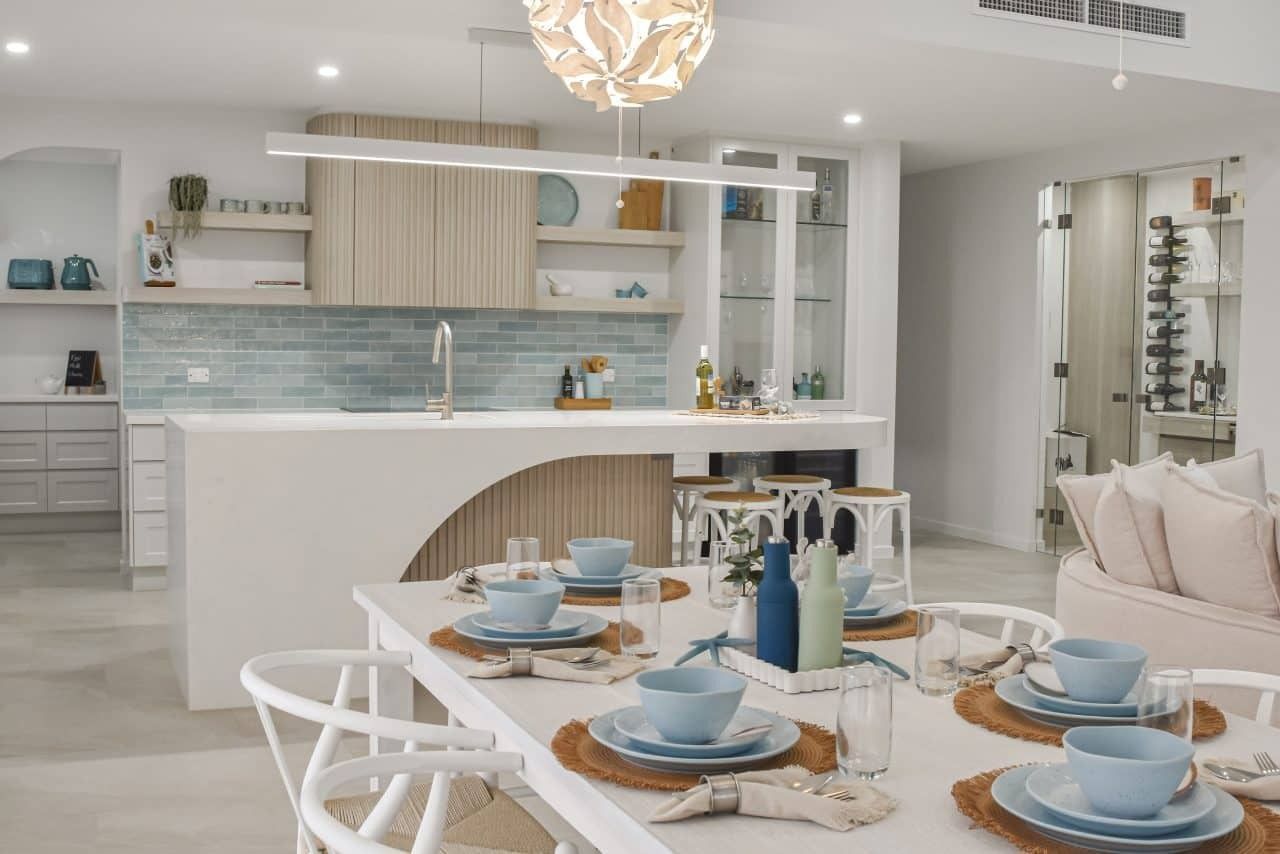 Bright open kitchen and dining area with white furniture, blue tableware, and warm pendant lighting