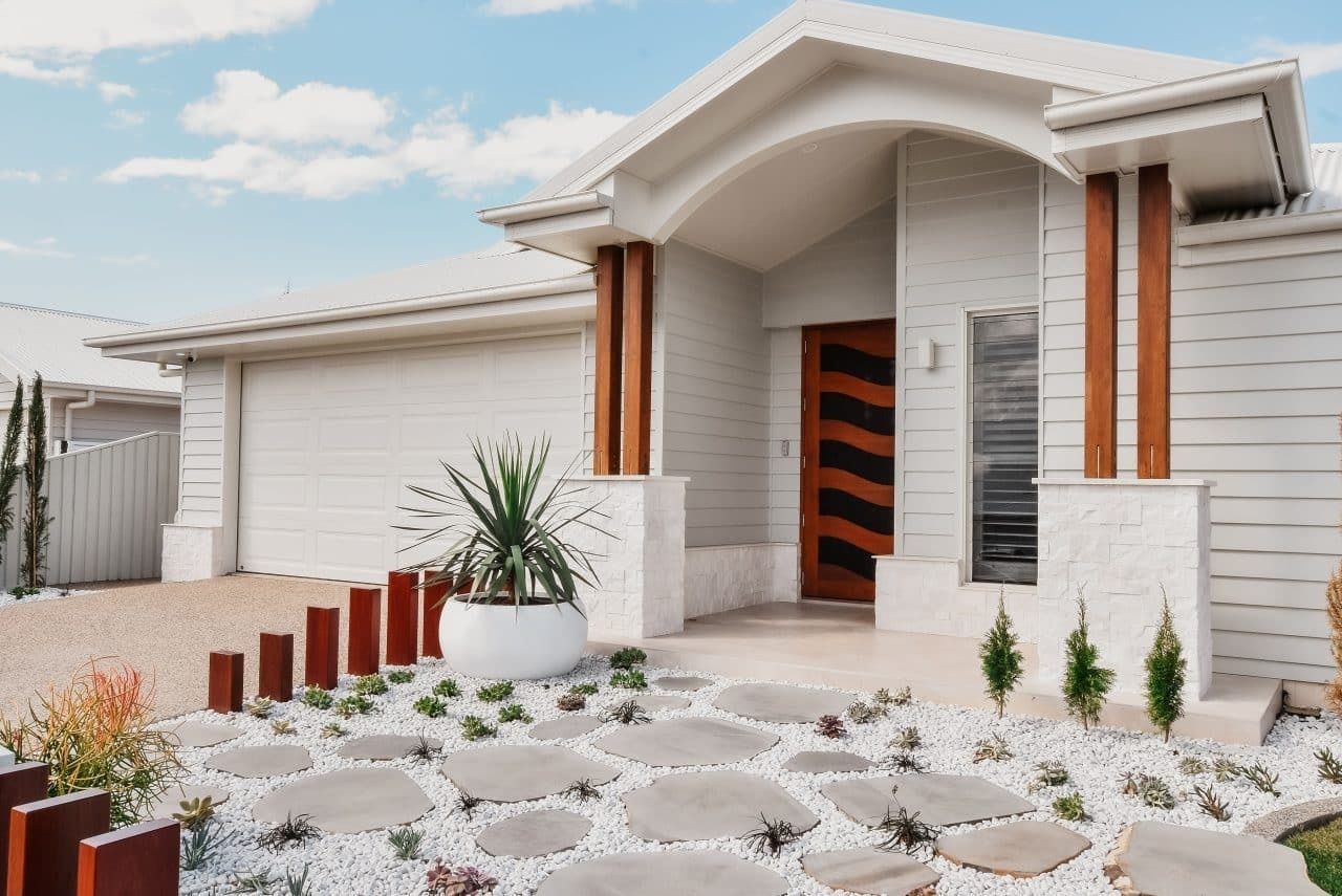 Modern white house exterior with a covered porch, stone walkway, and landscaped front yard
