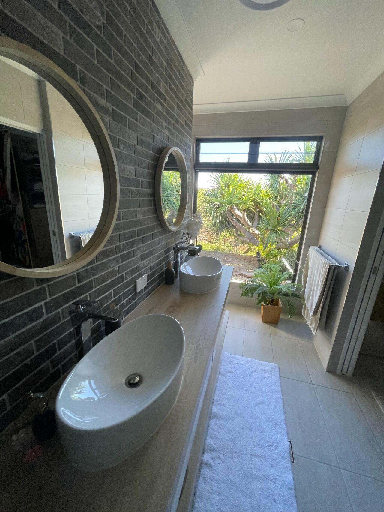 Modern bathroom with black tile wall, two sinks, mirrors, and a windowed view of greenery