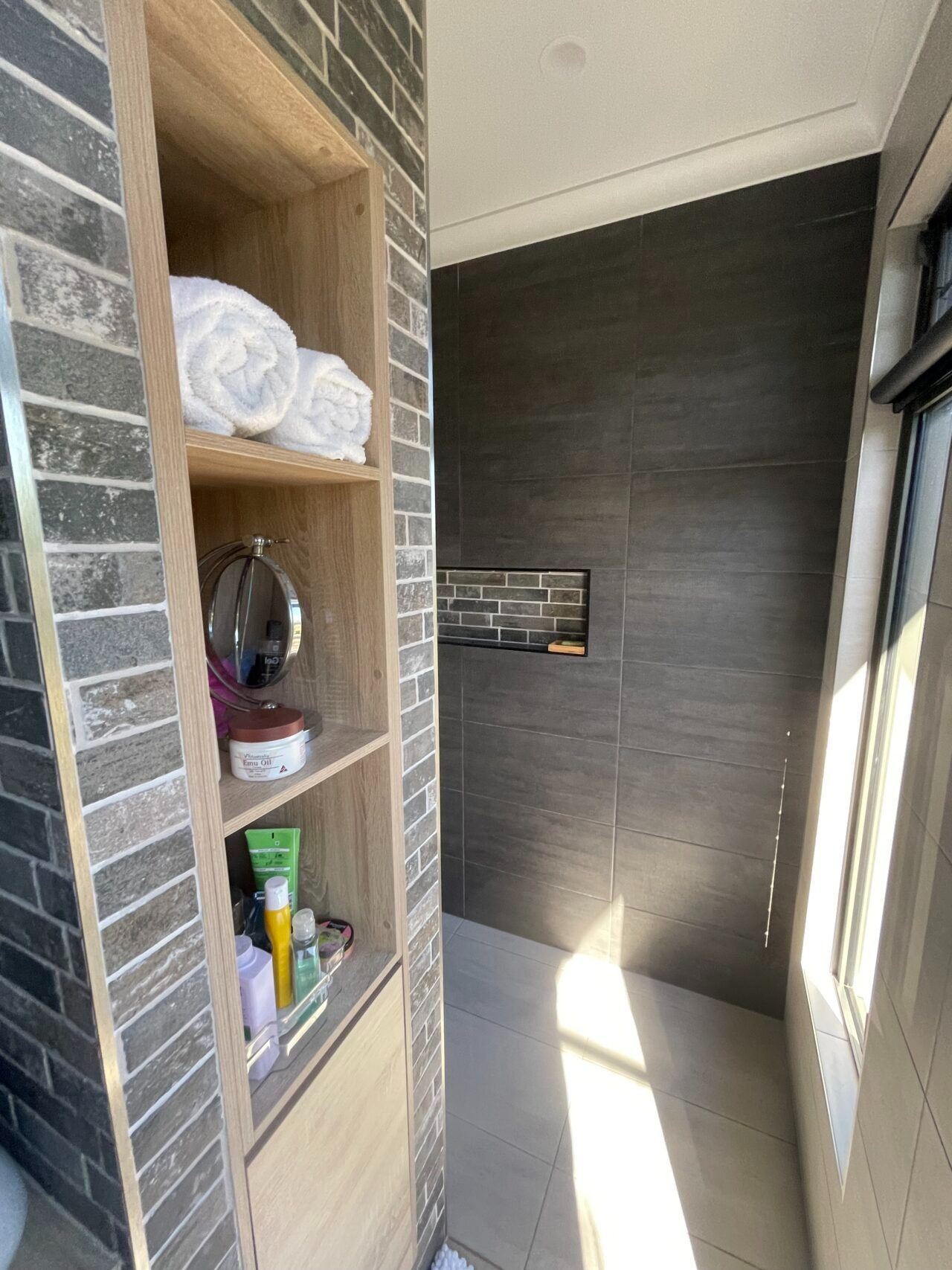 Narrow balcony with built-in shelves, brick wall, and sunlight on the floor; books and towels on the shelf
