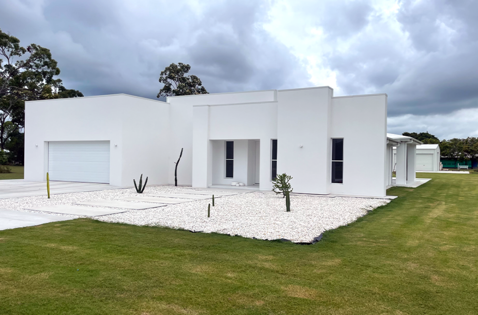 Modern white single-story house with a garage, white gravel yard, and green lawn under cloudy skies