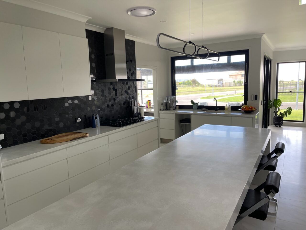 Modern kitchen with white cabinets, black backsplash, large island, and windows overlooking a yard