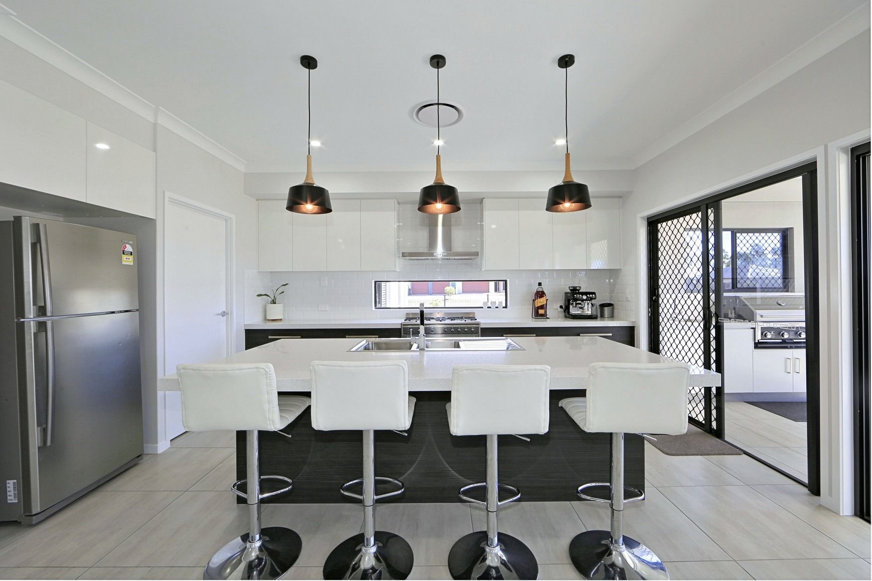 Modern white kitchen with island, pendant lights, barstools, and stainless steel fridge and appliances