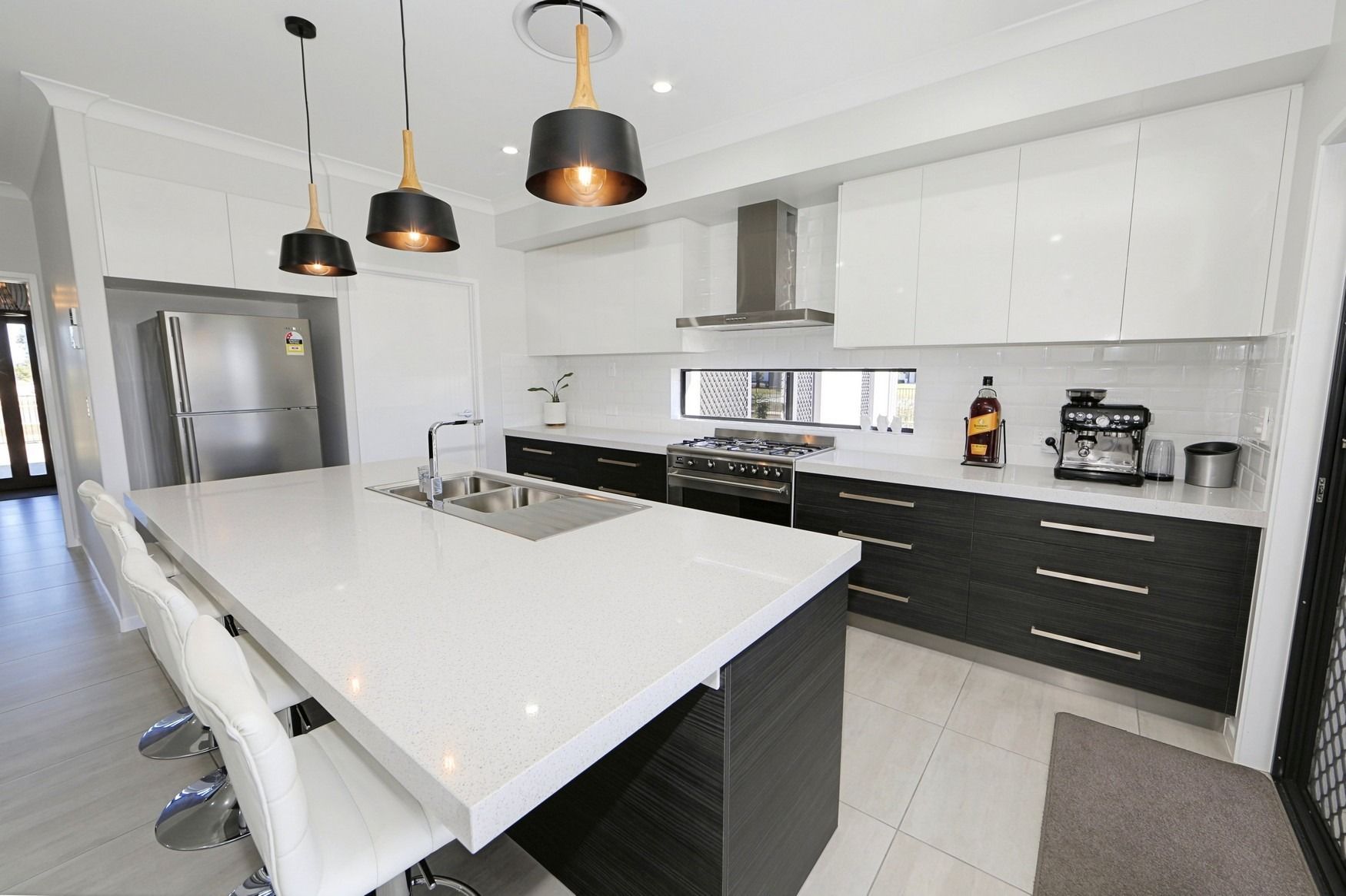 Modern white kitchen with black accents, island, pendant lights, stainless steel appliances, and dark lower cabinets