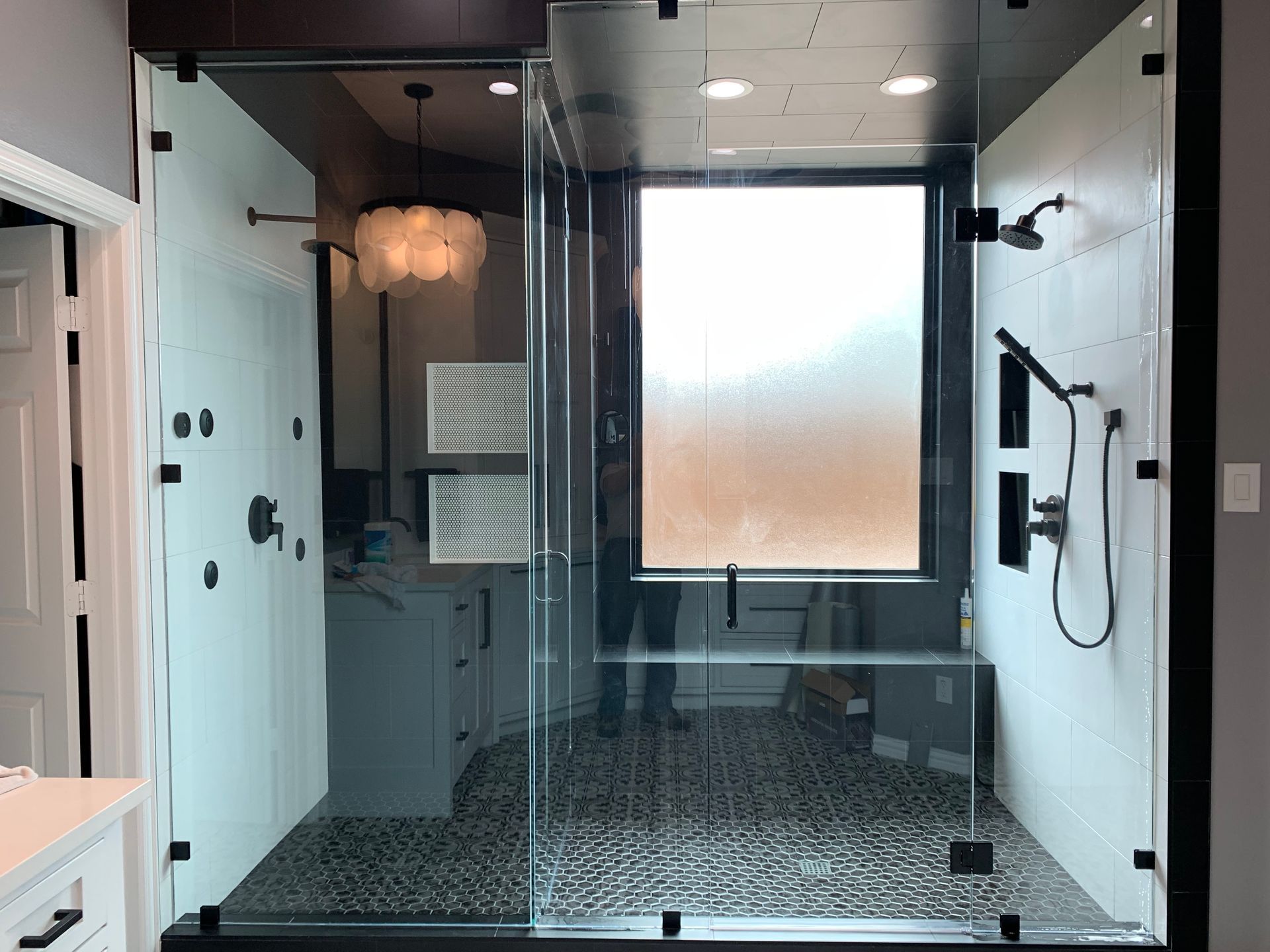 Modern walk-in shower with glass doors, dark fixtures, black and white tile, and a window.