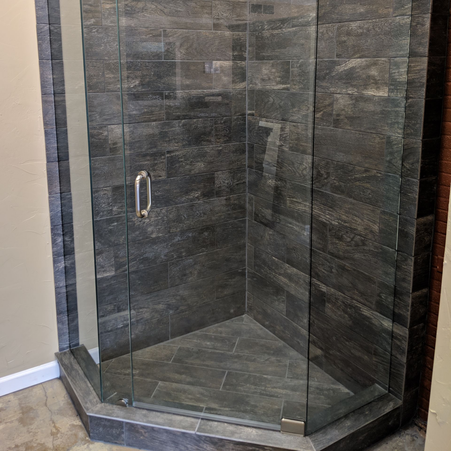 A glass-enclosed shower with dark gray tiled walls and floor, silver handle.