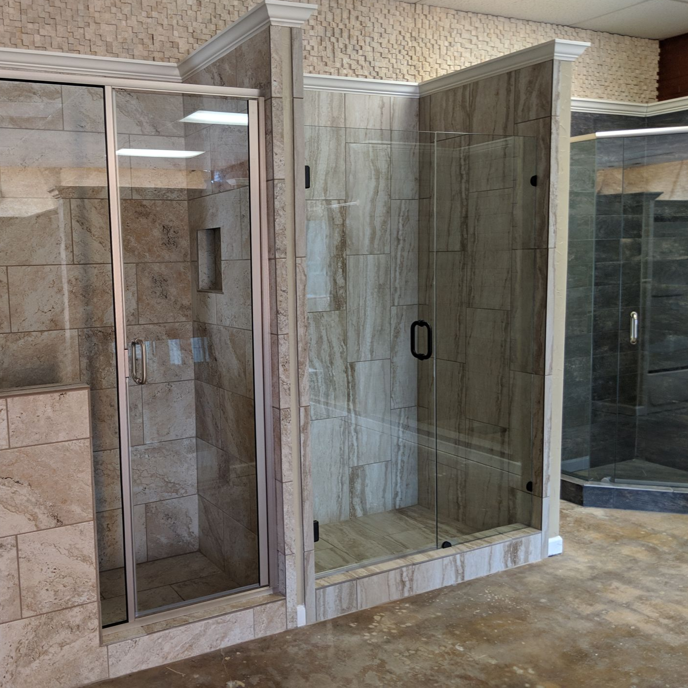 Shower stalls with glass doors and stone-like tile walls in a showroom.