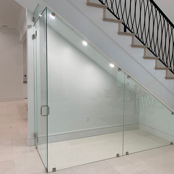 Glass-enclosed space under a staircase, with door and lights; white walls, tan stairs, black railing.