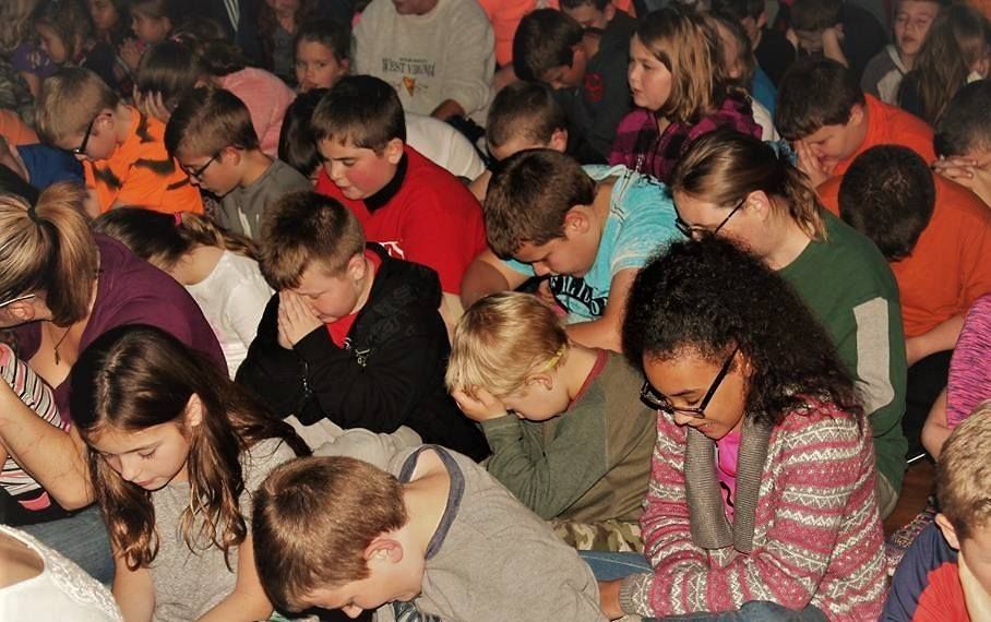 Group of students with heads bowed, possibly praying, in a room.