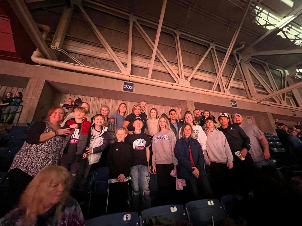 Group of people seated in an arena. Some are smiling, others looking at the camera. Rows of seats visible.
