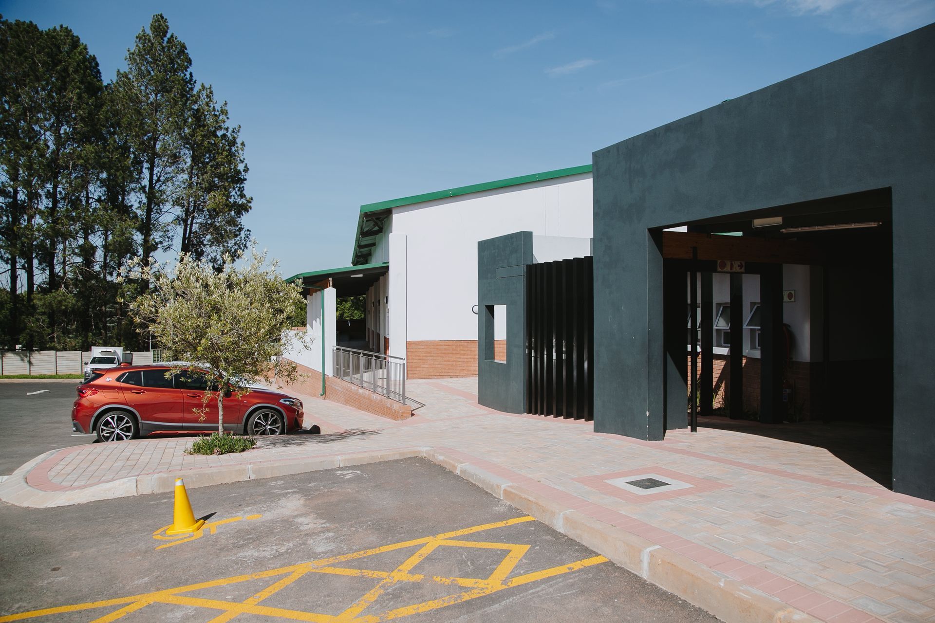 A red car is parked in a parking lot in front of a building.