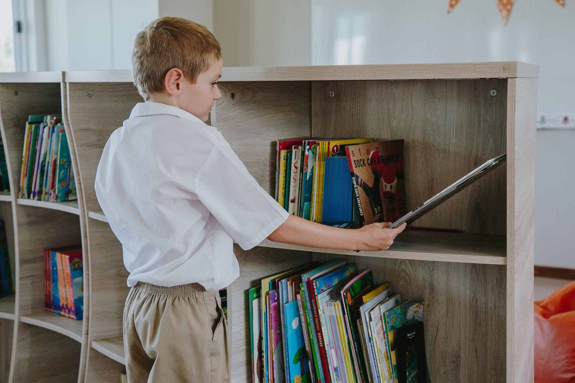 A young boy is looking at a book on a shelf in a library.