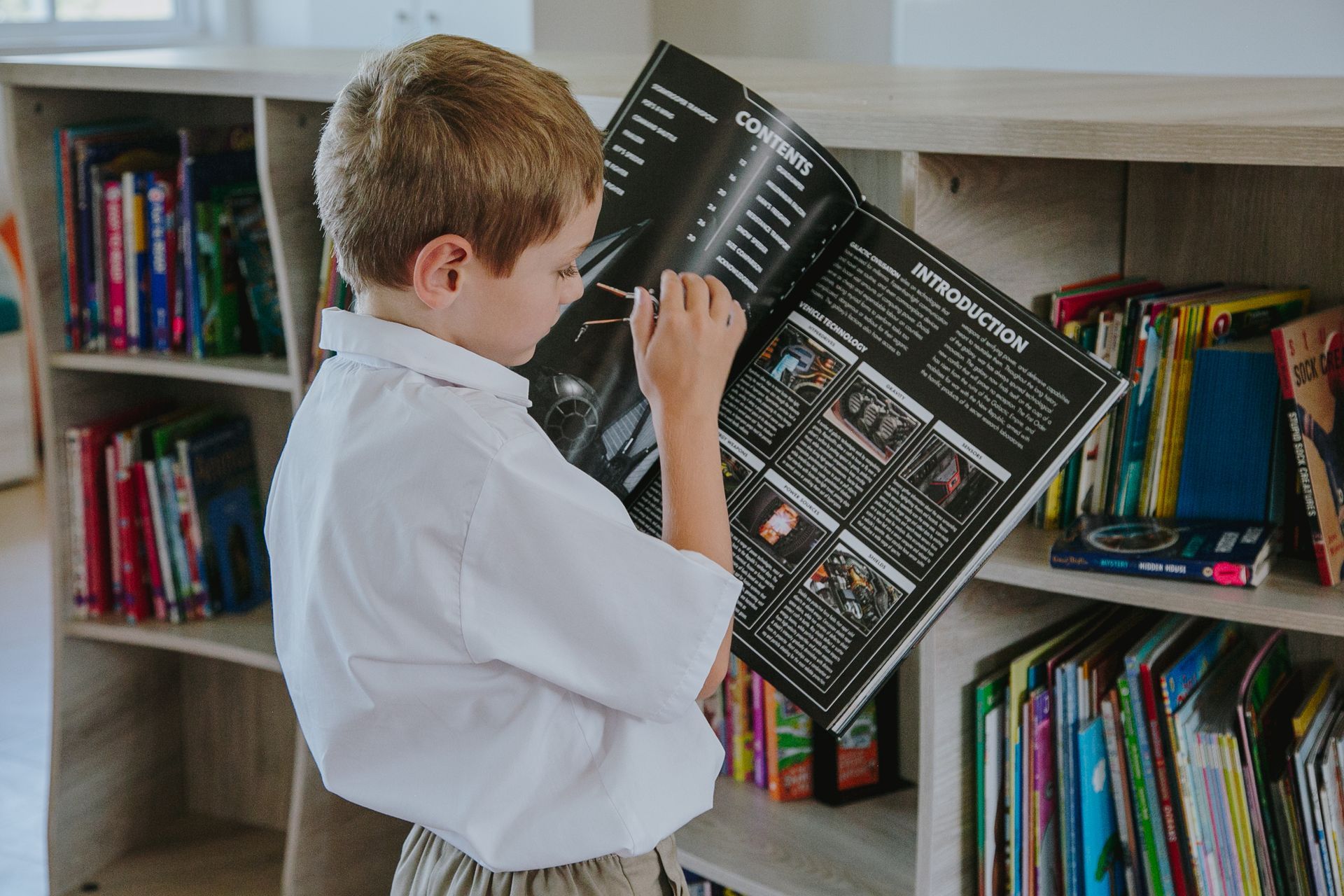 A young boy is reading a book in a library.
