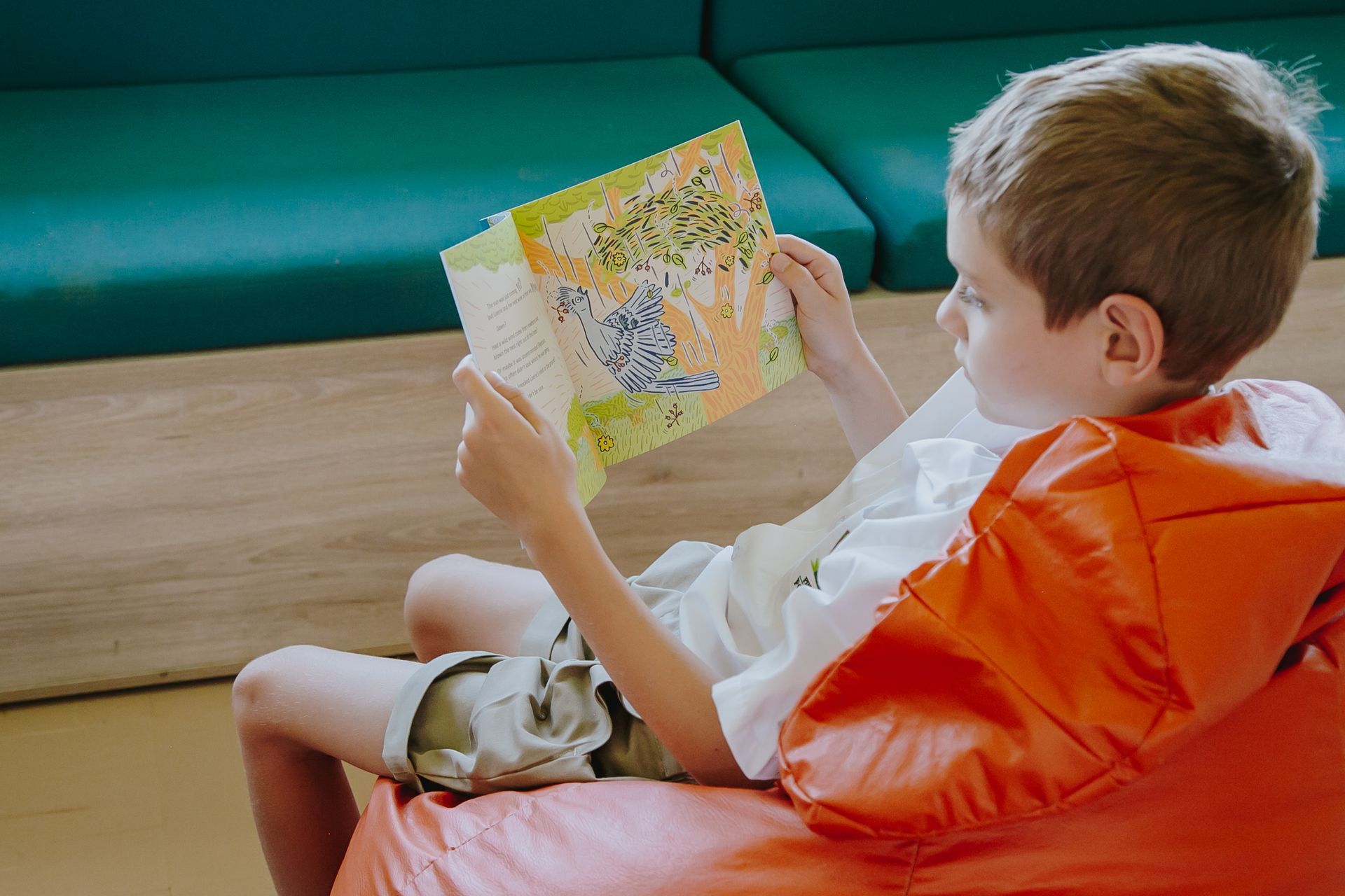 A young boy is sitting on a bean bag chair reading a book.