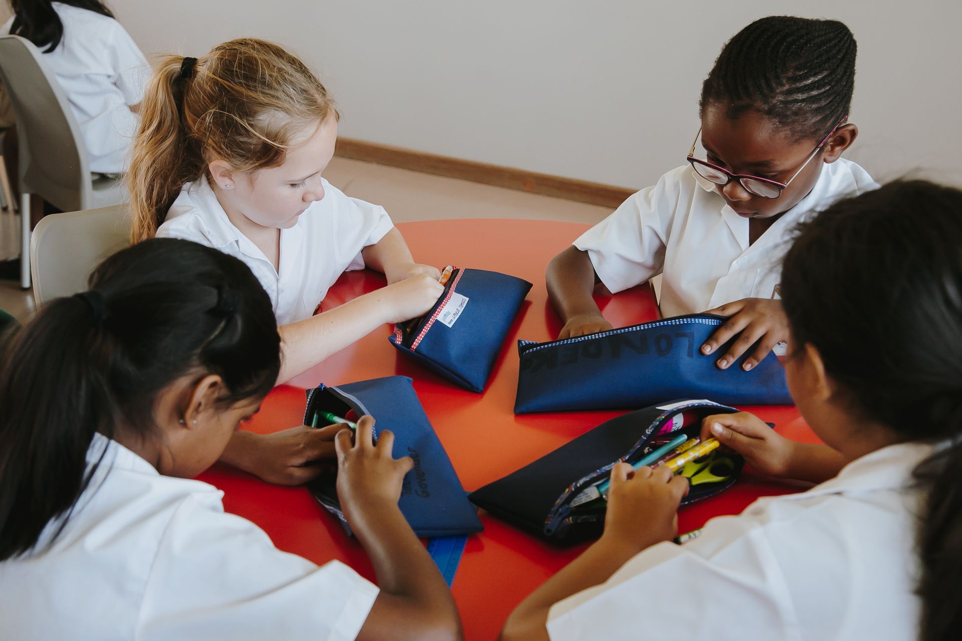 A group of young girls are sitting around a table with pencil cases.
