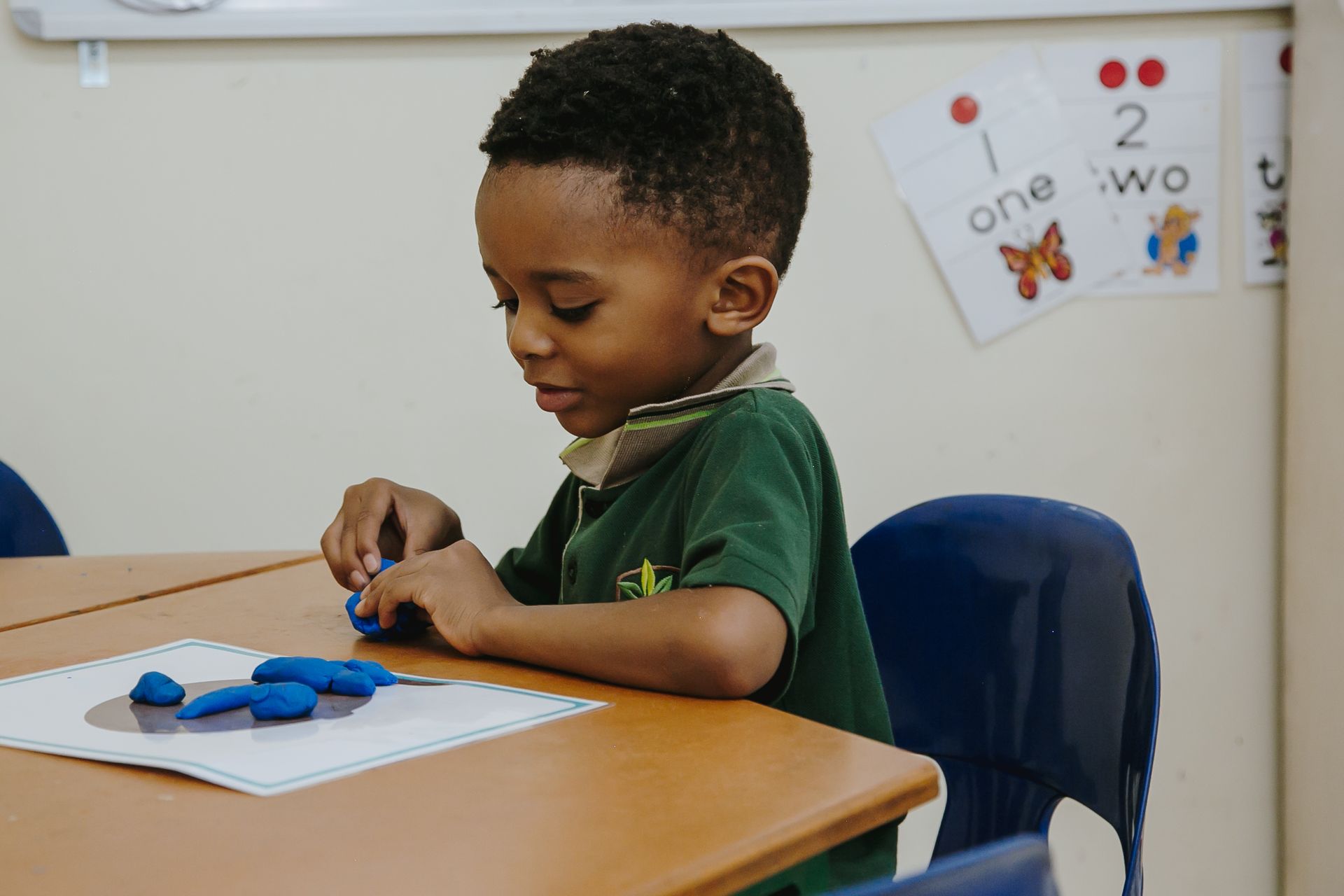 A young boy is sitting at a table playing with blue clay.