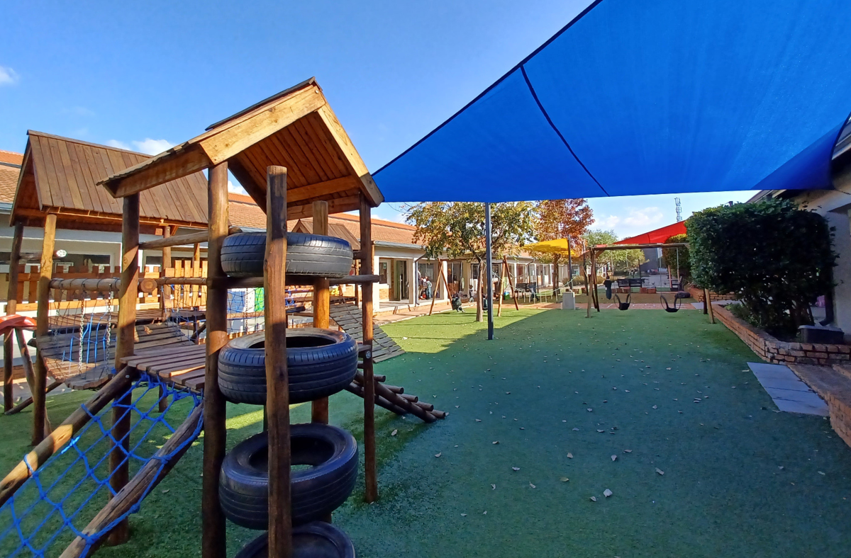 A playground with a blue umbrella and a wooden structure made out of tires.