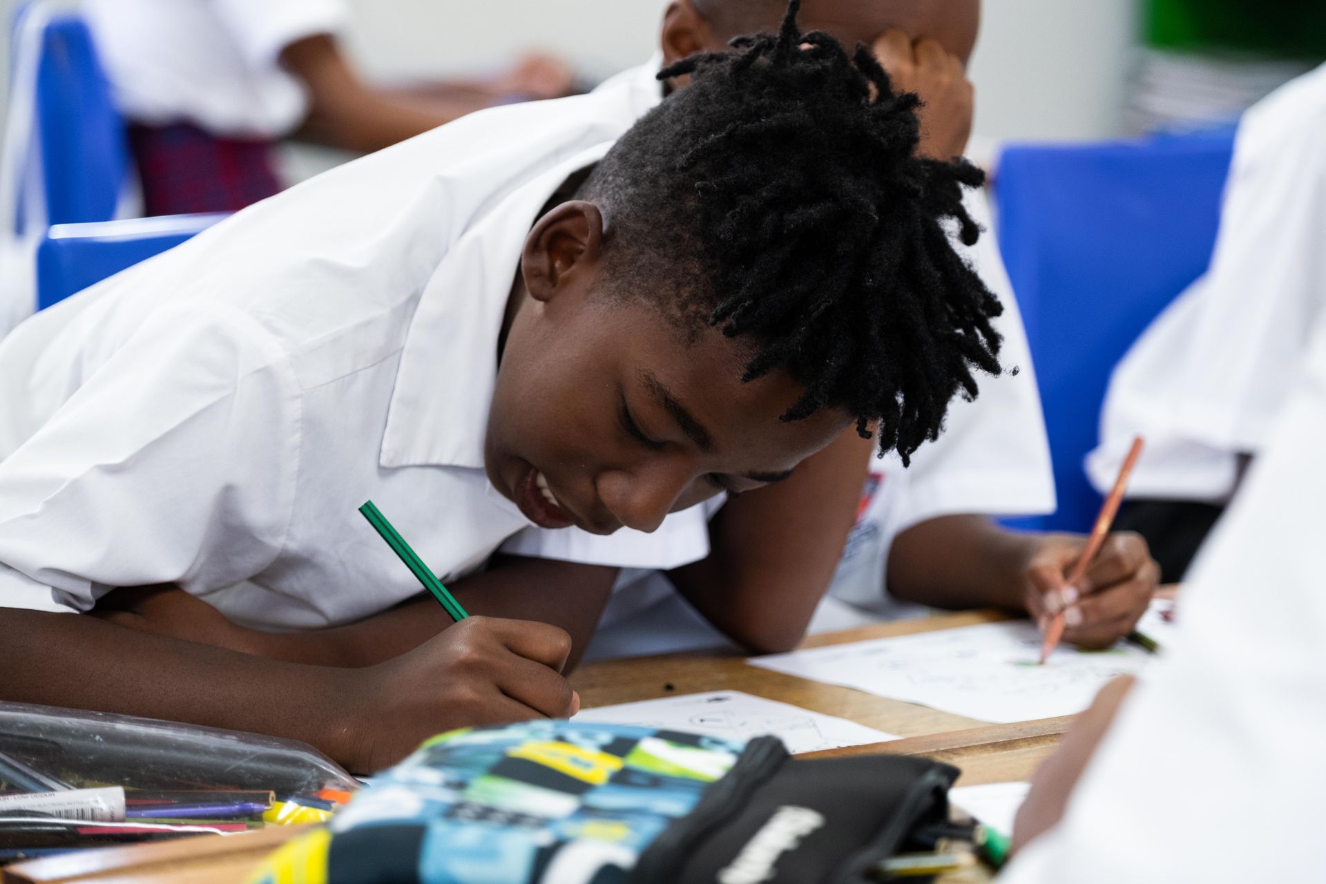 A young boy is sitting at a desk in a classroom writing on a piece of paper.