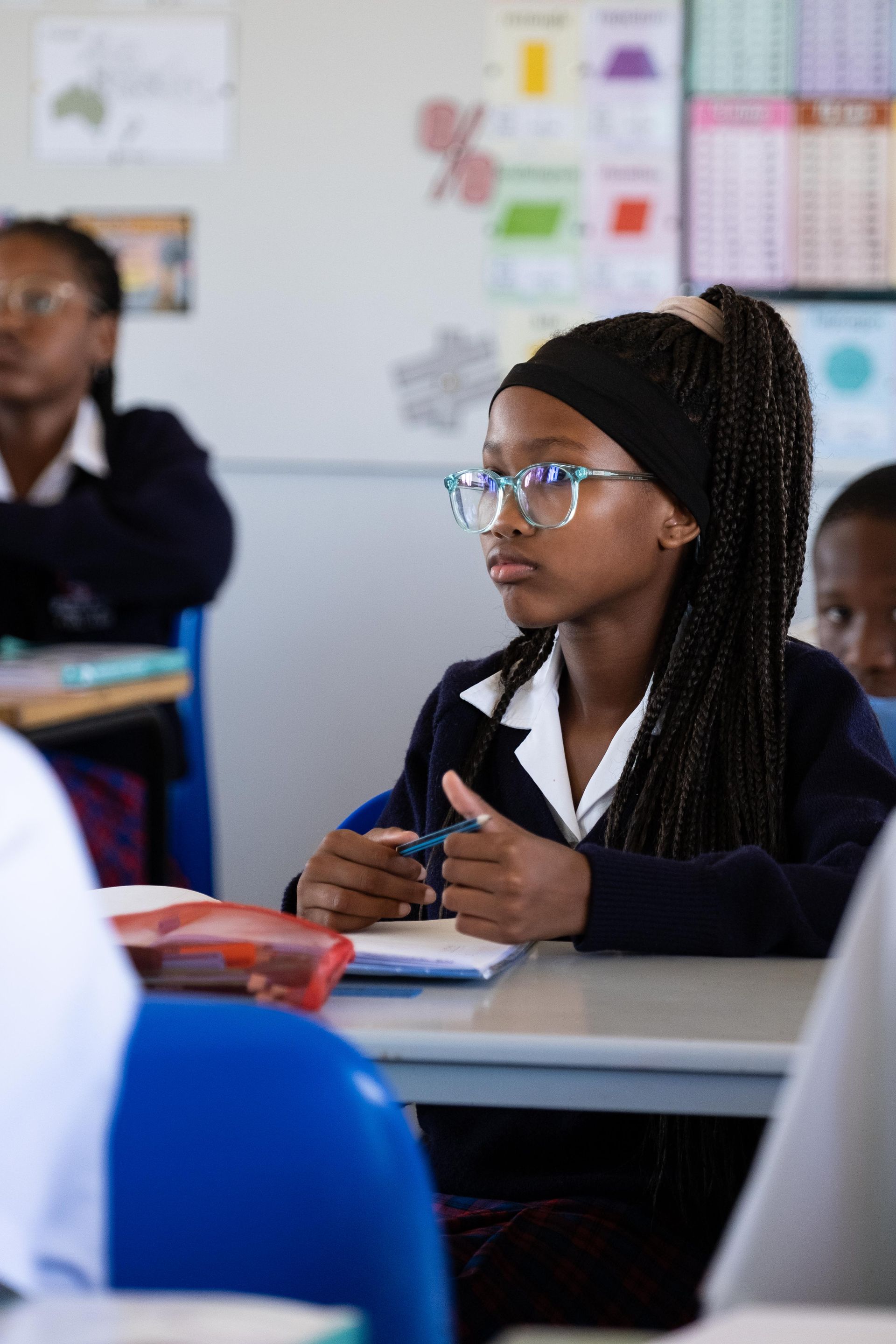 A young girl wearing glasses is sitting at a desk in a classroom.