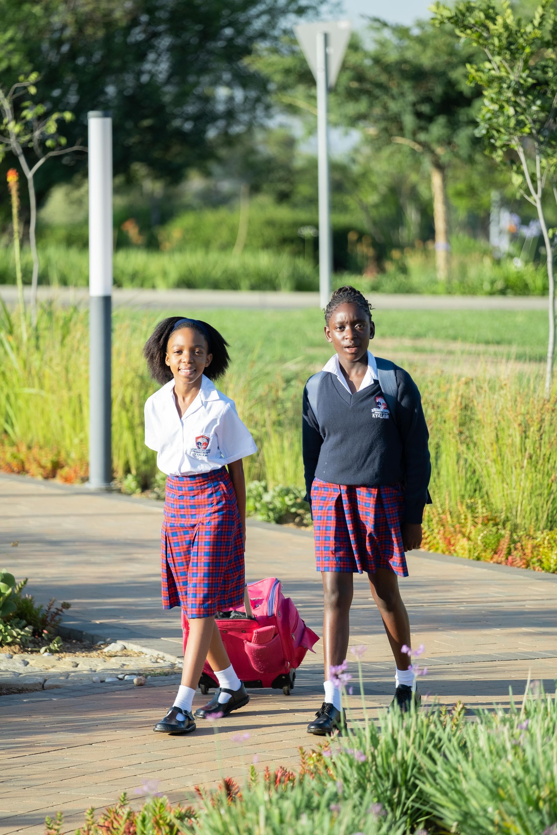 Two young girls in school uniforms are walking down a sidewalk.