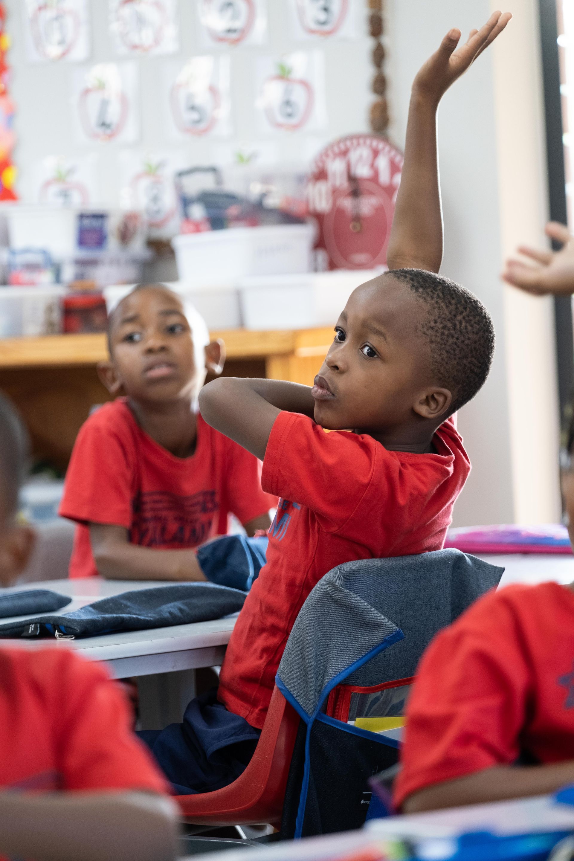 A young boy is raising his hand in a classroom to answer a question.