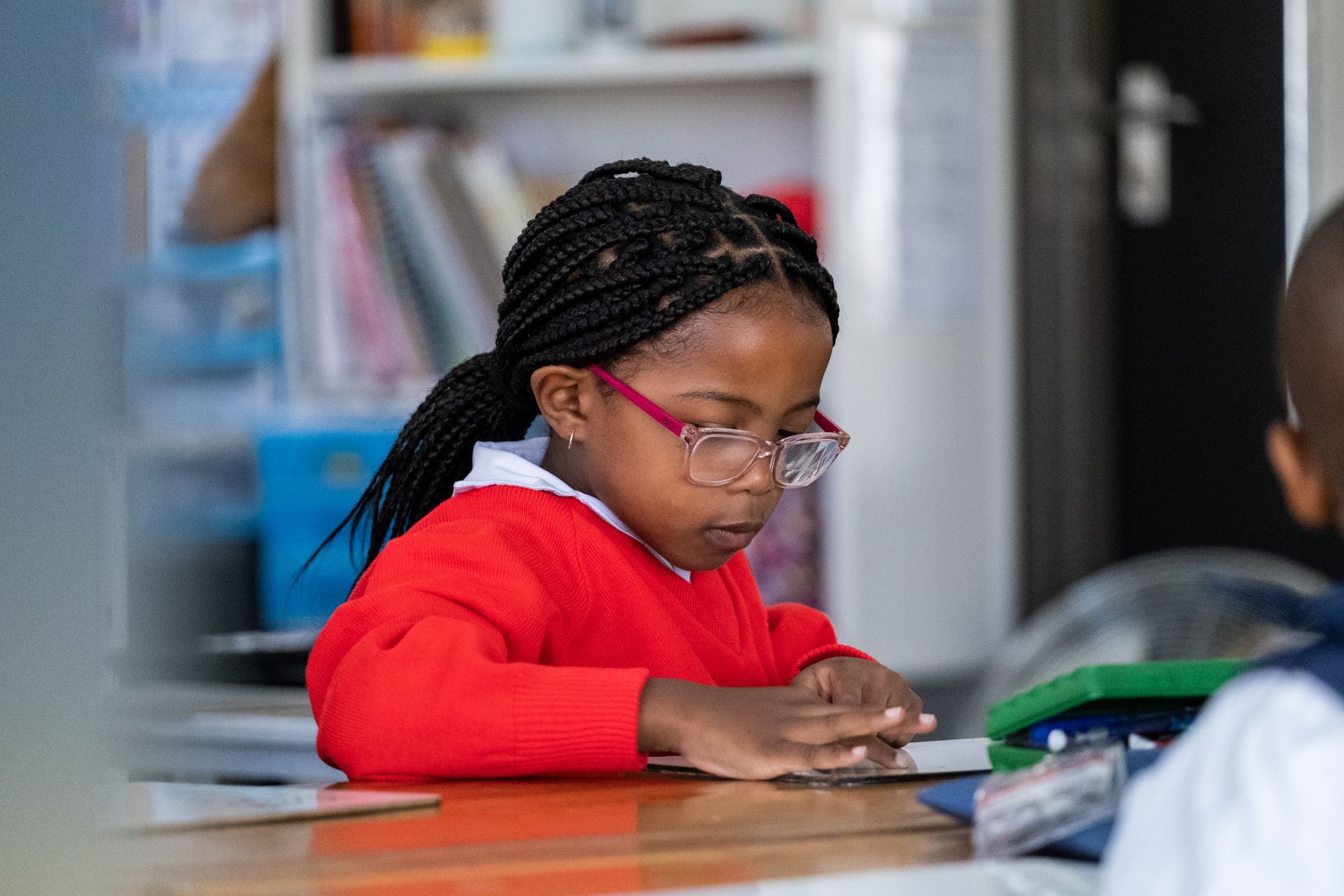 A young girl wearing glasses is sitting at a table in a classroom.