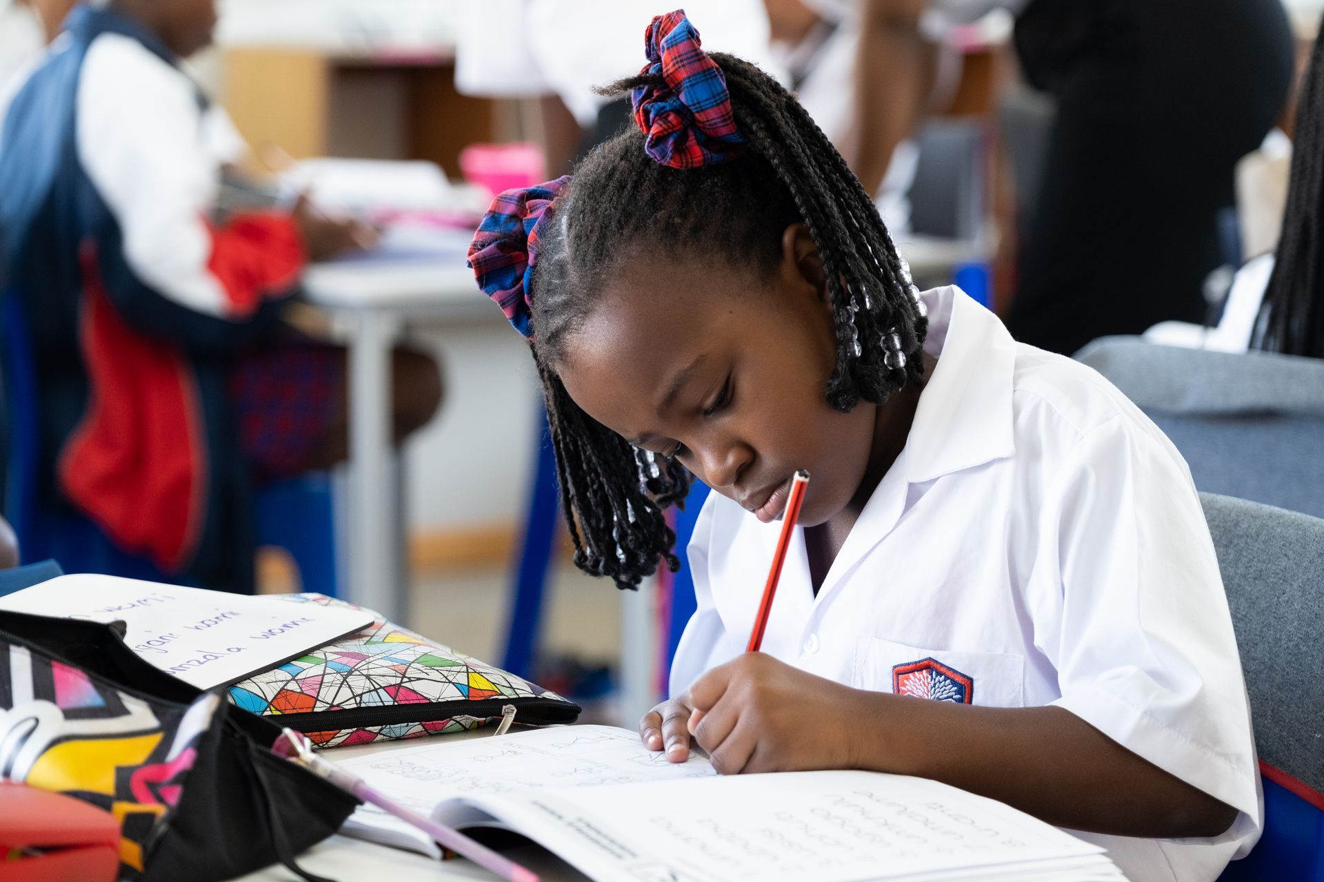 A young girl is sitting at a desk in a classroom writing in a notebook.