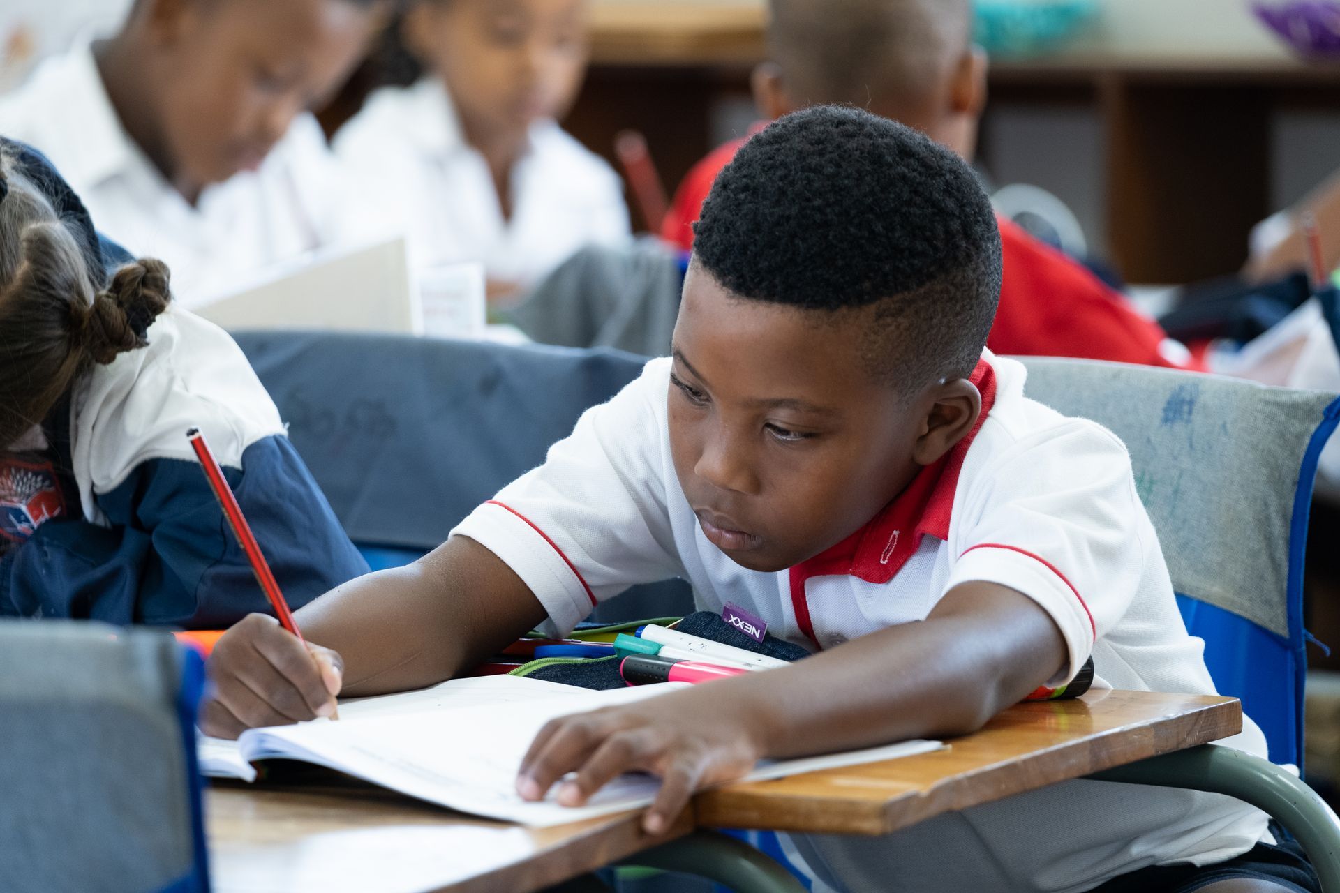 A young boy is sitting at a desk in a classroom writing in a notebook.