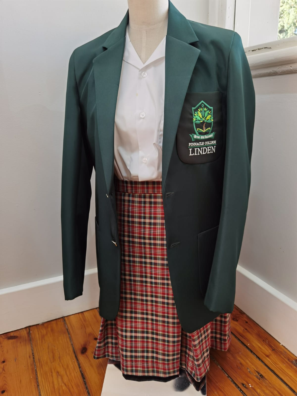 A green jacket and plaid skirt are on a mannequin.
