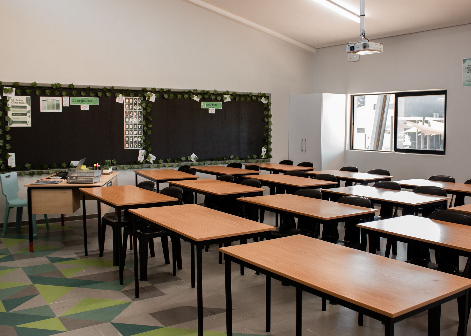 An empty classroom with wooden tables and chairs and a projector.