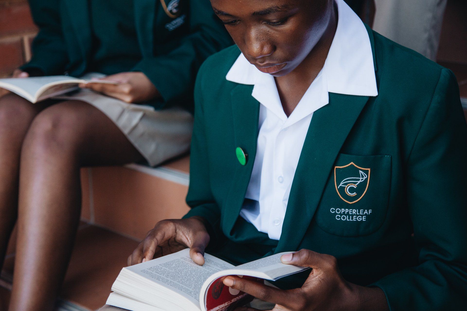 A girl in a green school uniform is reading a book.