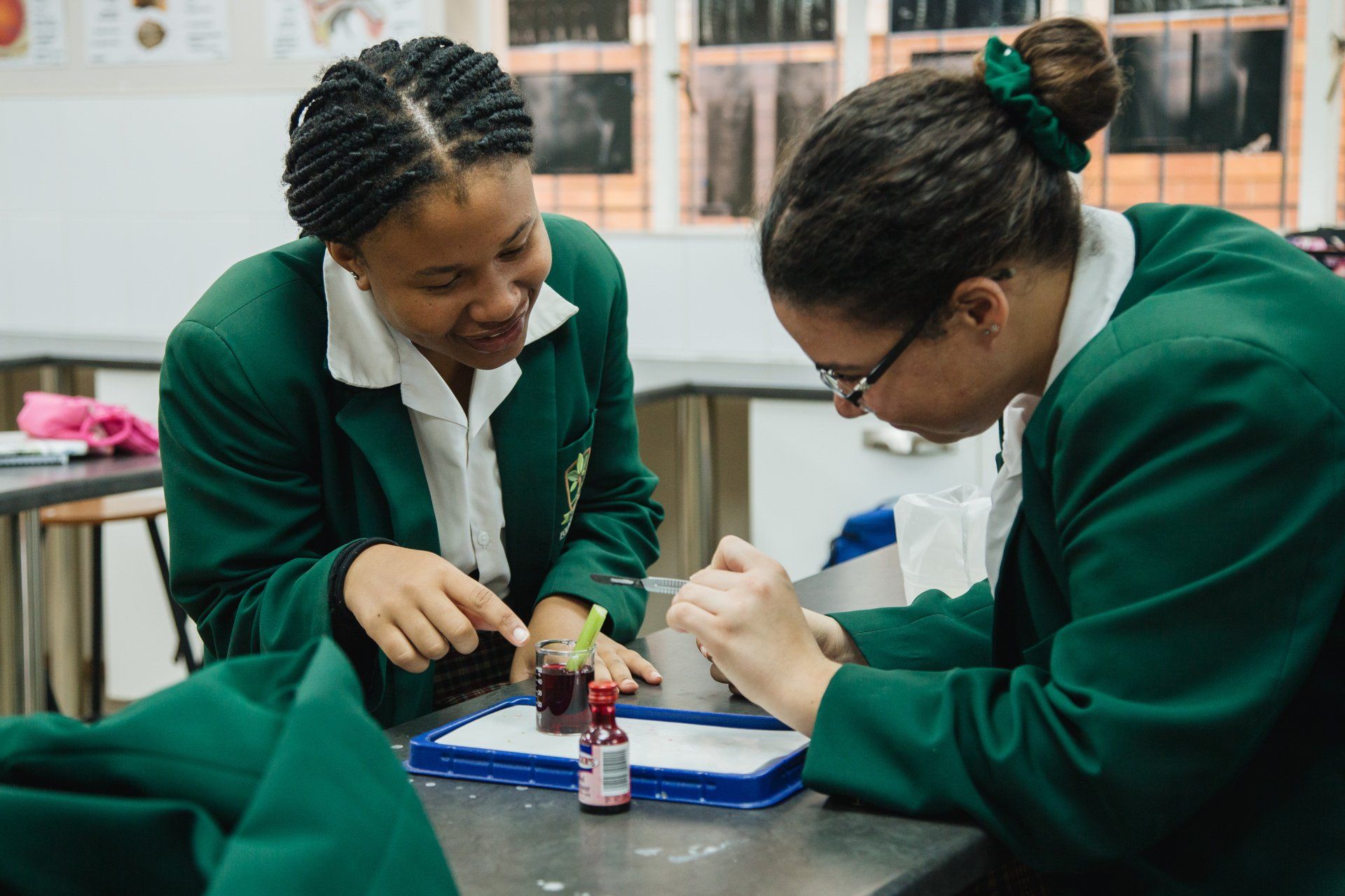 Two girls are sitting at a table in a classroom looking at something.