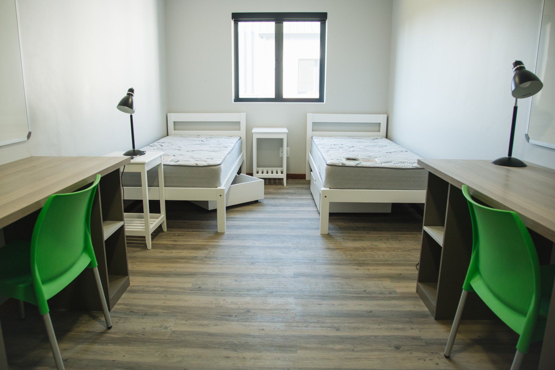 A bedroom with two beds , two desks , and two green chairs.