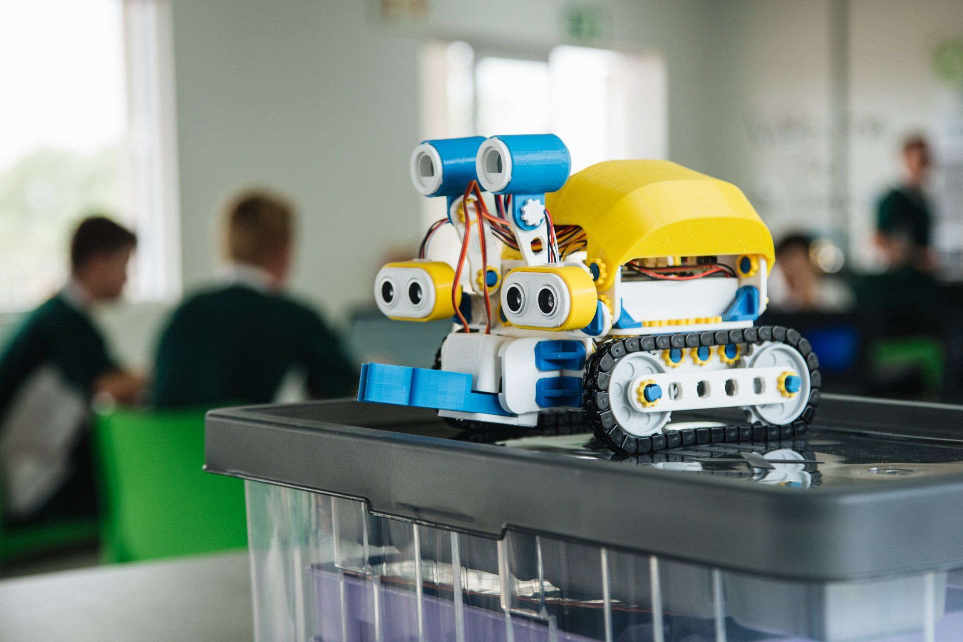 A toy robot is sitting on top of a plastic container in a classroom.