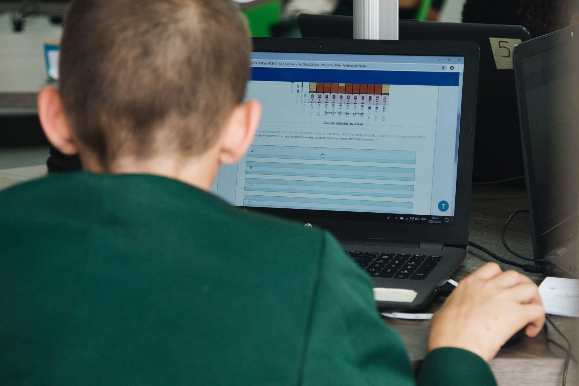 A young boy is sitting at a desk using a laptop computer.