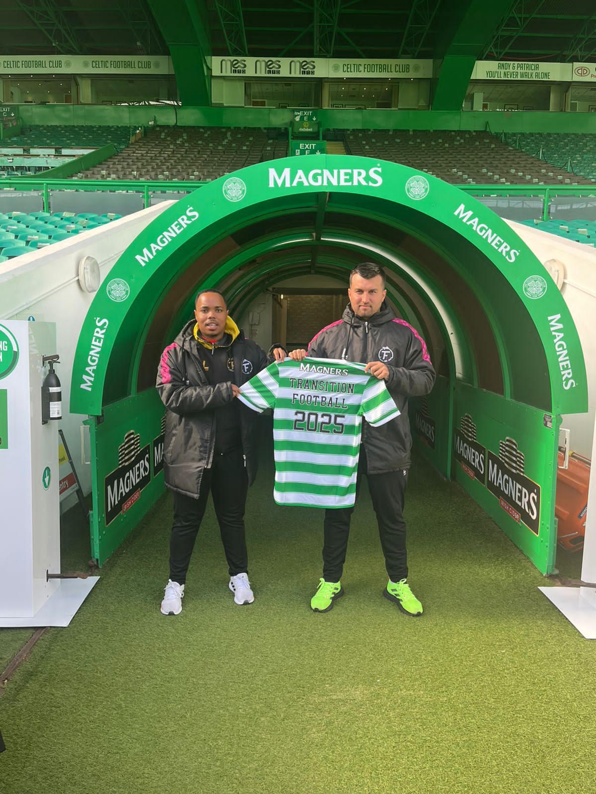 Two men are standing in a tunnel holding a soccer jersey.