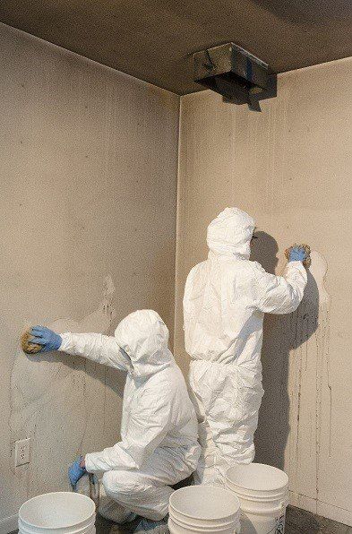 Two men in protective suits are cleaning a wall with a sponge.