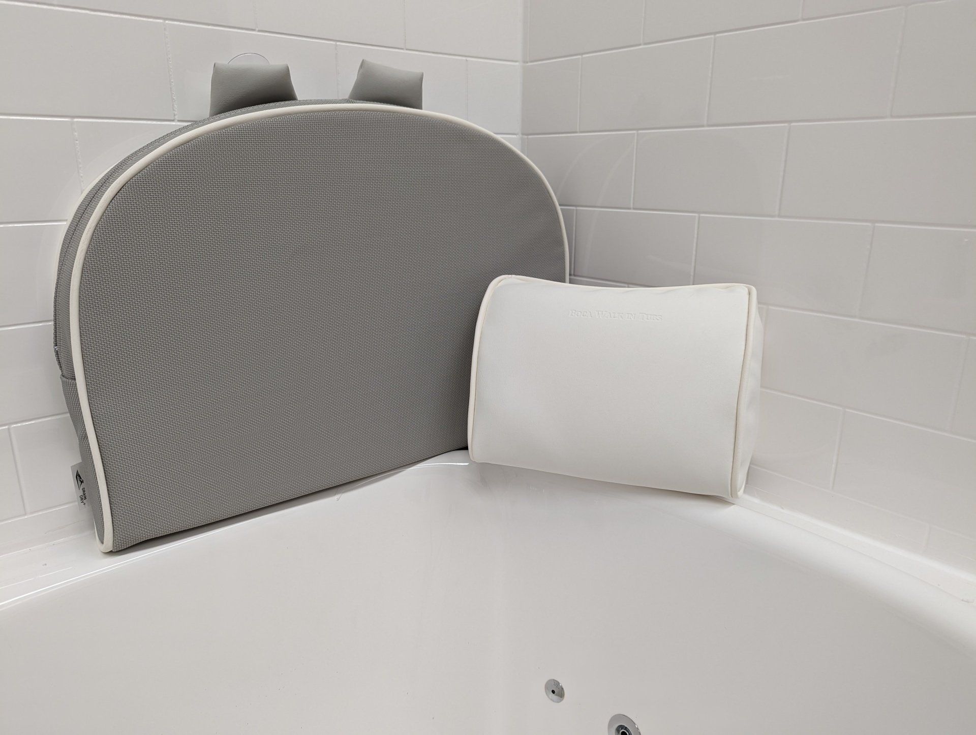 A gray arched bath cushion and a smaller white rectangular bath pillow attached to the edge of a white bathtub.