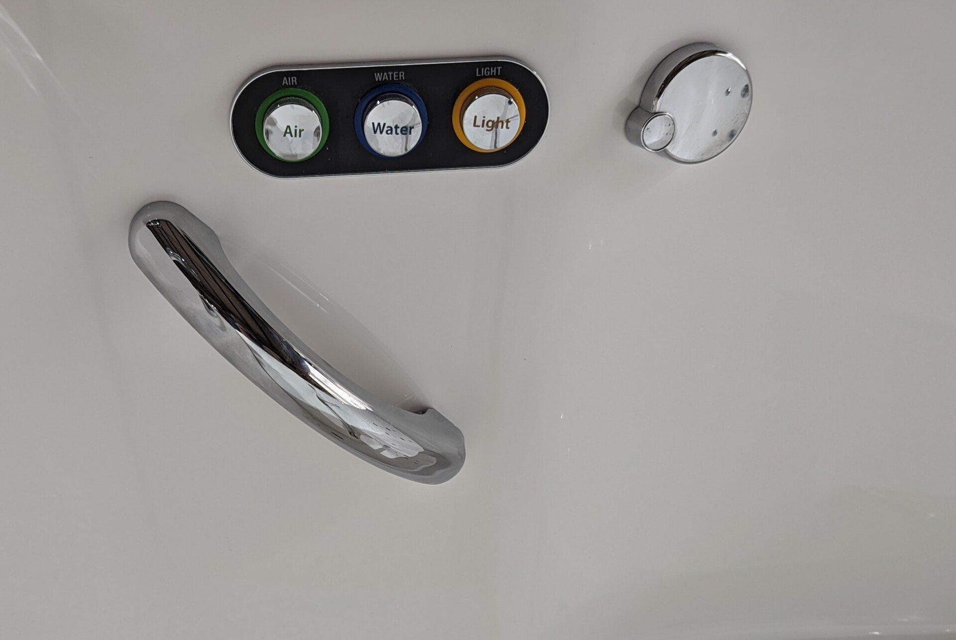 A chrome grab bar mounted on a white wall next to a control panel with green, blue, and yellow buttons and a dial.