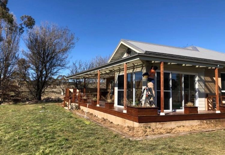 A man is standing on a ladder in front of a house with a porch. — Thomas Croker Constructions In Myrtleville, NSW