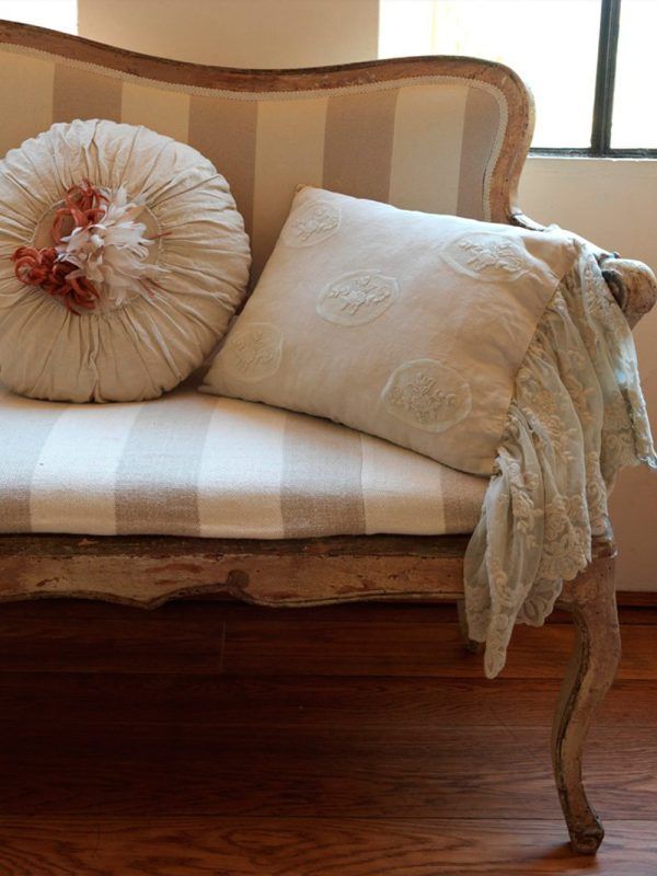 Divano a righe con cuscini rotondi e quadrati e una coperta in pizzo drappeggiata.