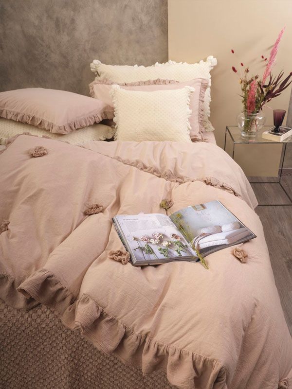 Letto con lenzuola rosa e cuscini decorativi, libro aperto.