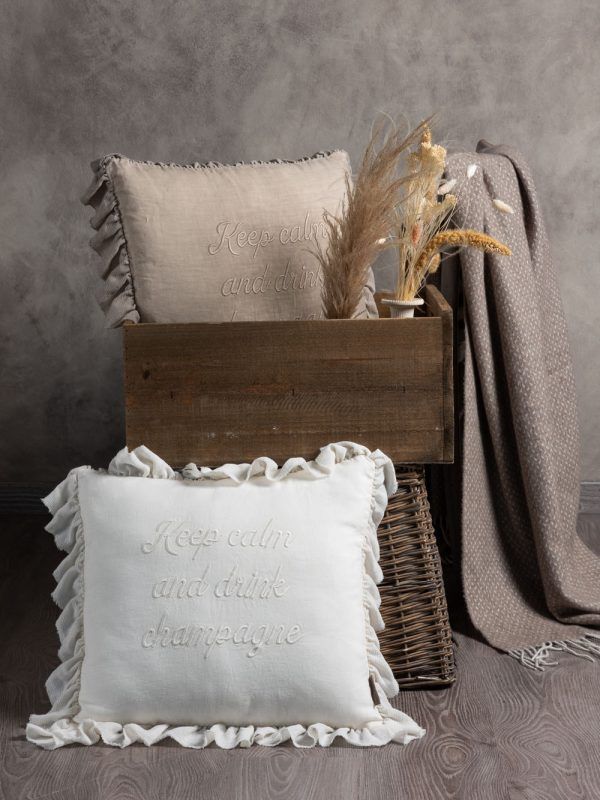 Due cuscini arricciati, uno bianco e uno beige, sono appoggiati davanti a una scatola di legno. Accanto a loro ci sono una coperta e dell'erba secca.