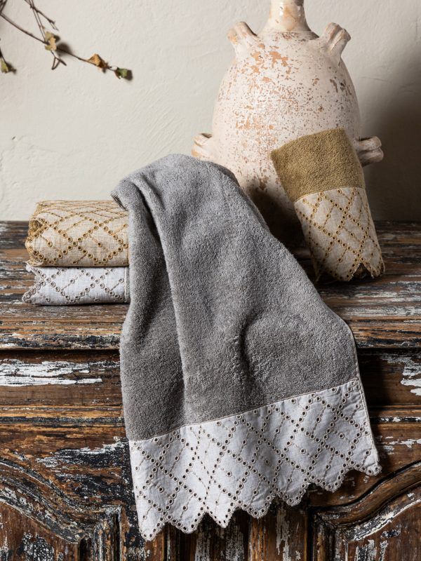 Asciugamani grigi e beige con motivo decorativo a rombi, piegati su una superficie rustica in legno con un vaso.