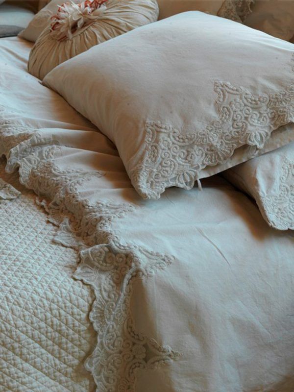 Letto con biancheria color crema, cuscini e trapunta inclusi, con delicate rifiniture in pizzo.