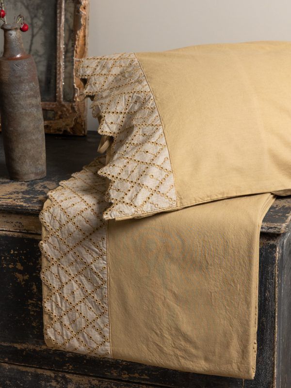 Cuscino marrone chiaro con bordo decorativo su una superficie di legno, decoro antico sullo sfondo.