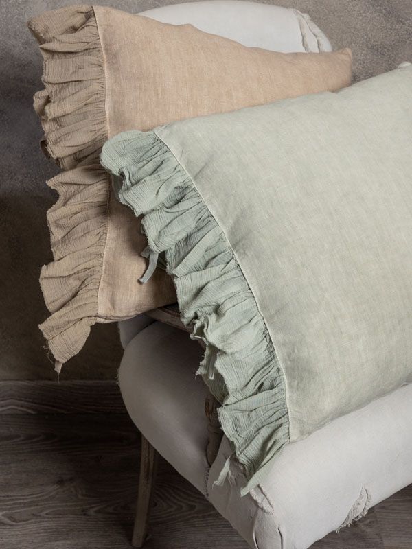 Due cuscini di lino con i bordi arricciati, uno beige e uno verde salvia, sono appoggiati su una sedia color crema.