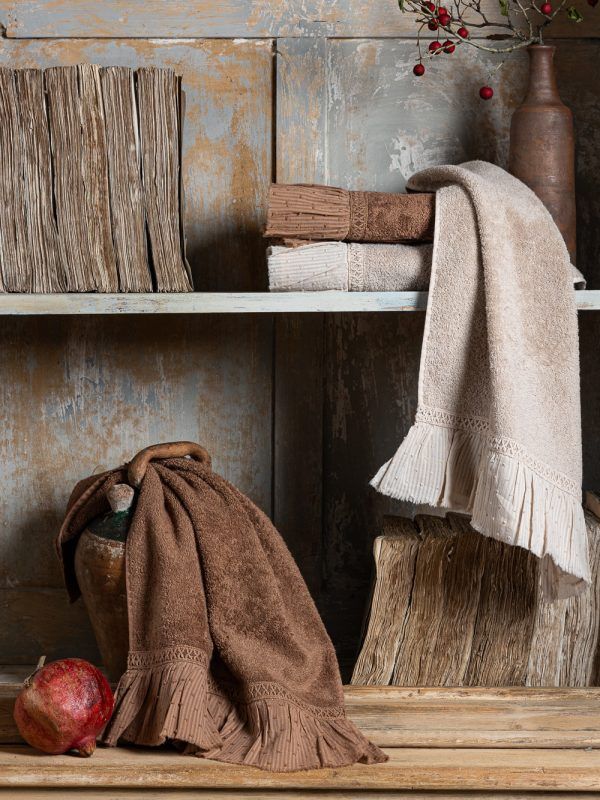 Asciugamani esposti su uno scaffale rustico in legno: uno è appoggiato su una bottiglia, l'altro ha il bordo sfrangiato.
